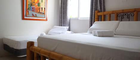 A hotel room with a large bed, a smaller bed, a wooden headboard, a window with curtains, and a painting on the wall.