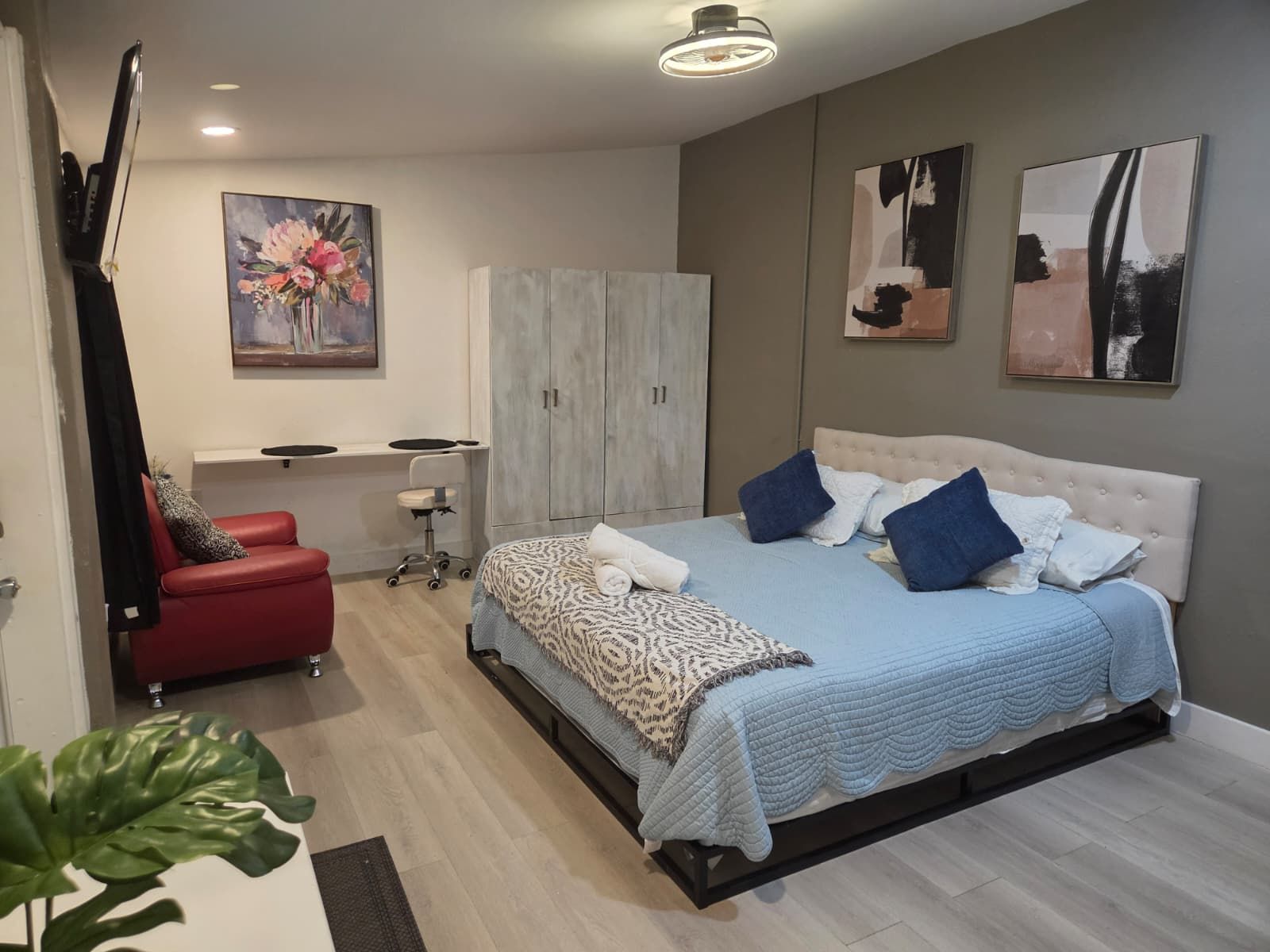 Quarto com cama, escrivaninha, cadeira, guarda-roupa e obras de arte nas paredes.
