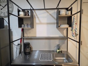 A compact kitchen with a coffee maker, a sink, and shelves with kitchenware. - Cozy studio apartment in tranquil Cutler Bay with AC and parking available (Cutler Bay)
