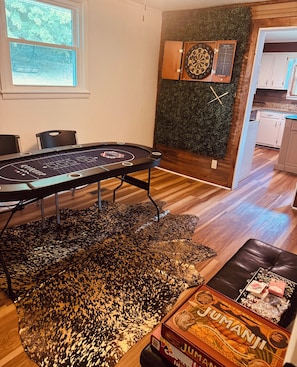 Una habitación con dardos, una mesa con un juego y una caja de Jumanji.