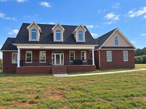 A two-story brick house with a front porch, a garage, and a well-maintained lawn.