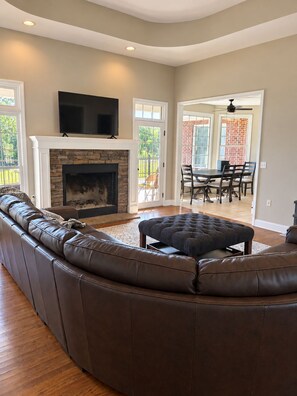 A living room with a stone fireplace, a large leather sectional sofa, and a flat-screen TV mounted above the fireplace.