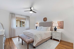 A bedroom with a bed, bedside tables, a bench, a ceiling fan, and a window with curtains. - Walk to Oxford Square | Sleeps 8 | Perfect for Ole Miss Getaways! (Oxford)