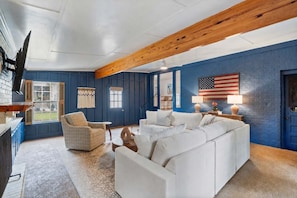 A room with a blue wall, a white sofa, a plaid armchair, and a wooden ceiling beam. - Walk to Oxford Square | Sleeps 8 | Perfect for Ole Miss Getaways! (Oxford)