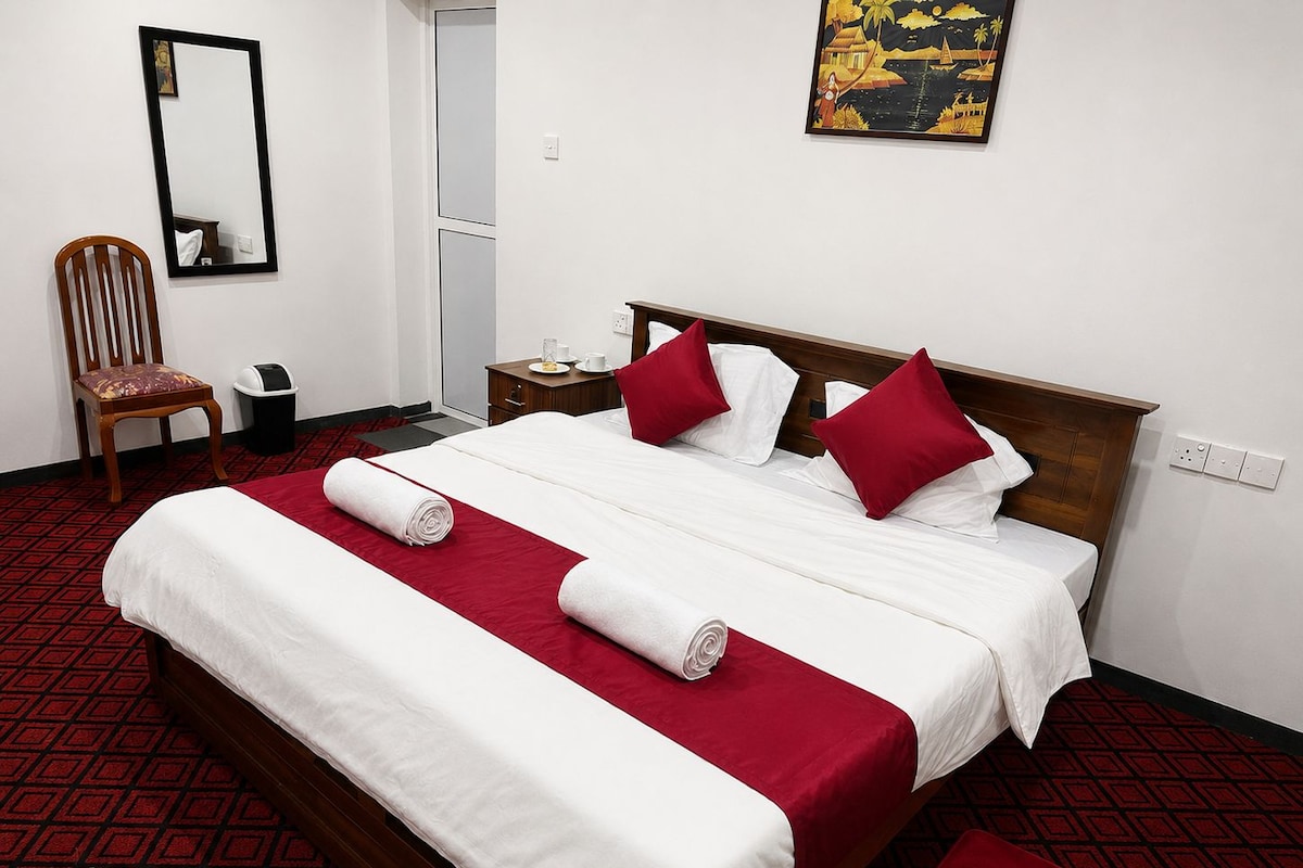 A hotel room with a large bed, two pillows, a chair, a nightstand, a mirror, and a painting on the wall.