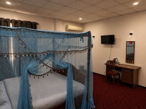 Una habitación de hotel con una cama, un escritorio, una silla, un televisor y un equipo de aire acondicionado.