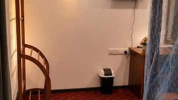 Een kamer met een rood kamerbreed tapijt, een aan de muur bevestigde televisie, een kleine prullenbak en een houten stoel.