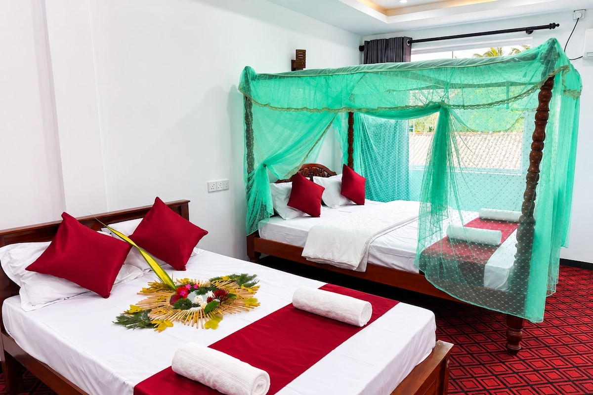 A hotel room with two beds, each with a canopy, red pillows, and a floral arrangement on the bed.
