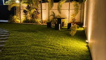 Un espacio exterior bien iluminado con un césped cuidado, una mesa y varias plantas en macetas.