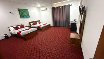 Una habitación de hotel con dos camas, una alfombra roja, un cuadro en la pared y un televisor sobre un mueble.