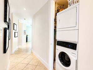 A laundry room with a washing machine and dryer, a tiled floor, and a hallway leading to another room. - Sapphire 1104 - By GISO Vacation Rentals (South Padre Island)