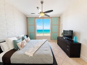A bedroom with a bed, a television, a ceiling fan, and a view of the ocean. - Sapphire 1104 - By GISO Vacation Rentals (South Padre Island)
