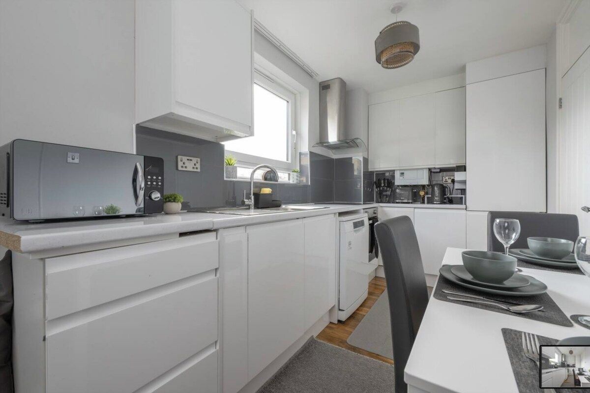 A modern kitchen with white cabinetry, a built-in microwave, and a dining area with a table set for two.