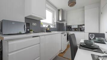 A modern kitchen with white cabinetry, a built-in microwave, and a dining area with a table set for two.