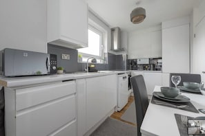 A modern kitchen with white cabinetry, a built-in microwave, and a dining area with a table set for two. - 3BR Flat in the heart of Bromley | Near Station|ST (London)