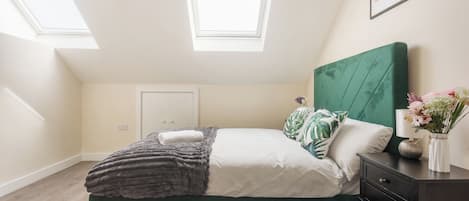 Un dormitorio con una cama tapizada en verde, una puerta blanca y un tragaluz.