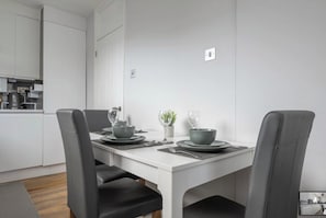 A modern dining area with a white table, grey chairs, and a minimalist design. - 3BR Flat in the heart of Bromley | Near Station|ST (London)