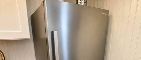 A stainless steel refrigerator with a built-in vegetable peeler and a potted plant on top.
