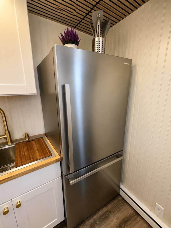 A stainless steel refrigerator with a built-in vegetable peeler and a potted plant on top.