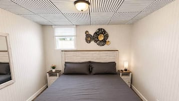Quarto com estrutura de cama de madeira, duas mesas de cabeceira, relógio na parede e janela com persianas.