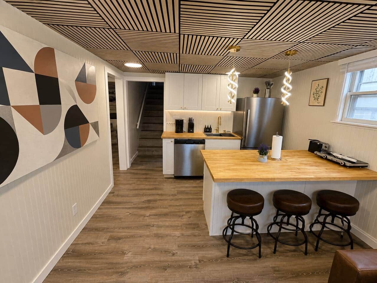 Une cuisine moderne avec un îlot central en bois, des tabourets de bar et un réfrigérateur en acier inoxydable.