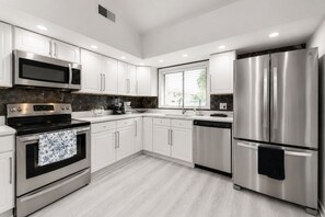 A modern kitchen with stainless steel appliances, white cabinetry, and a window providing natural light. - Orlando Hub: Cozy Suburban Oasis / 25 Mins to Theme Parks  &Airport (Orlando)