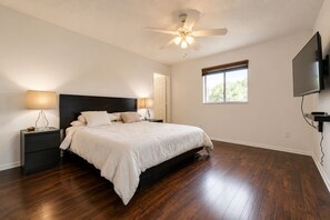 Una camera da letto con un letto, comodini, una ventola a soffitto, una finestra e una TV montata a parete.