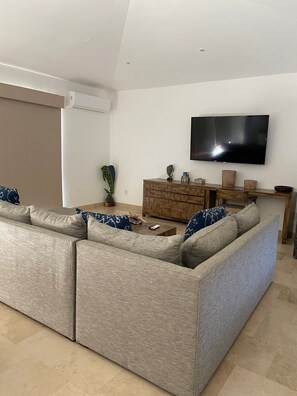 Ein Wohnzimmer mit einem großen Modulsofa, einem flachbildfernseher an der Wand und einem Couchtisch aus Holz.