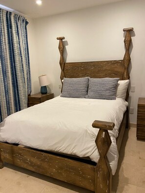 A bed with a wooden frame and white bedding, a bedside table with a lamp, and a curtain. - Charming 3-bedroom Modern Mexican house in a Exclusive Copala  Cabo San Lucas (Cabo San Lucas)
