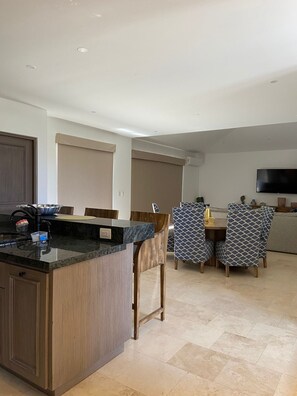 A modern kitchen with a central island, dining area with patterned chairs, and a flat-screen TV mounted on the wall. - Charming 3-bedroom Modern Mexican house in a Exclusive Copala  Cabo San Lucas (Cabo San Lucas)