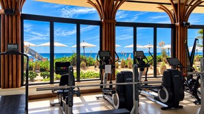 A gym with exercise equipment and large windows overlooking a beach. - Charming 3-bedroom Modern Mexican house in a Exclusive Copala  Cabo San Lucas (Cabo San Lucas)