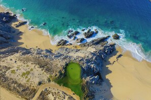 An aerial view of a coastal area with a sandy beach, rocky shoreline, and a green golf course. - Charming 3-bedroom Modern Mexican house in a Exclusive Copala  Cabo San Lucas (Cabo San Lucas)
