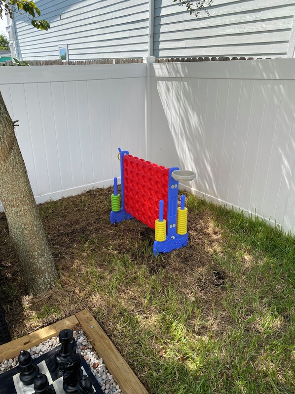 Un patio trasero con cerca blanca, un árbol y una estructura de juego roja y azul.