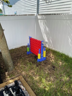 A backyard with a white fence, a tree, and a red and blue play structure.