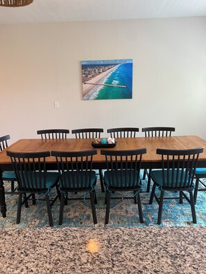 Een eetgedeelte met een houten tafel en zwarte stoelen, een vloerkleed en een schilderij van een strand.