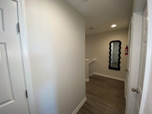A hallway with a white door on the left, a white wall, and a wooden floor.
