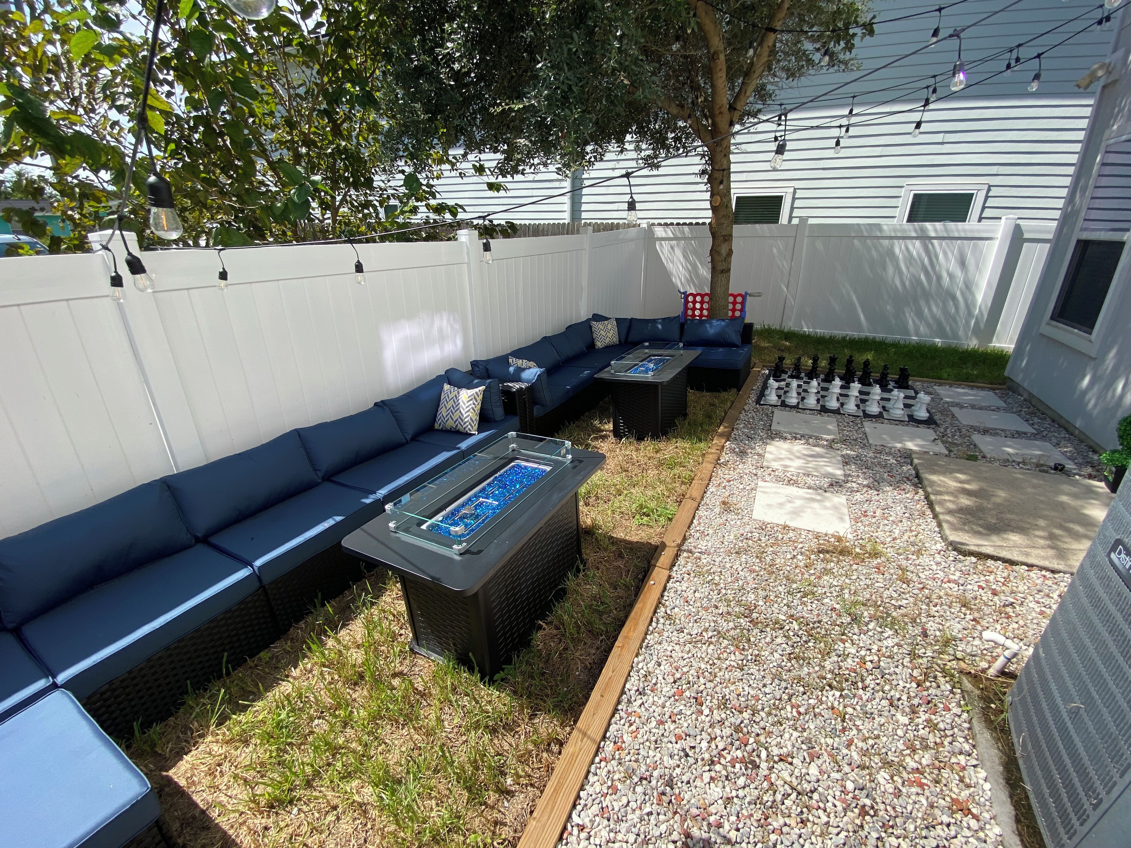 A backyard with a blue outdoor sofa, a glass-top coffee table, and a chessboard.