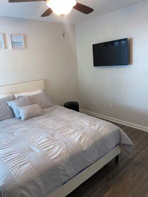A bedroom with a bed, a ceiling fan, a wall-mounted TV, and a small bedside table.