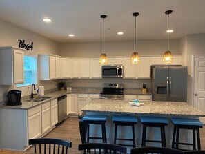 A modern kitchen with white cabinets, granite countertops, stainless steel appliances, and pendant lighting. - Jax Beach Vacation Stay, 4 bathrooms, 5-bedroom, 2 fire pits, and 2 balconies (Jacksonville Beach)