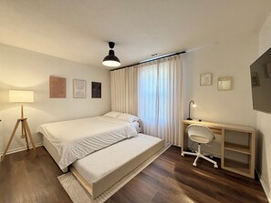 Un dormitorio con cama, escritorio, silla, lámpara y cortinas.