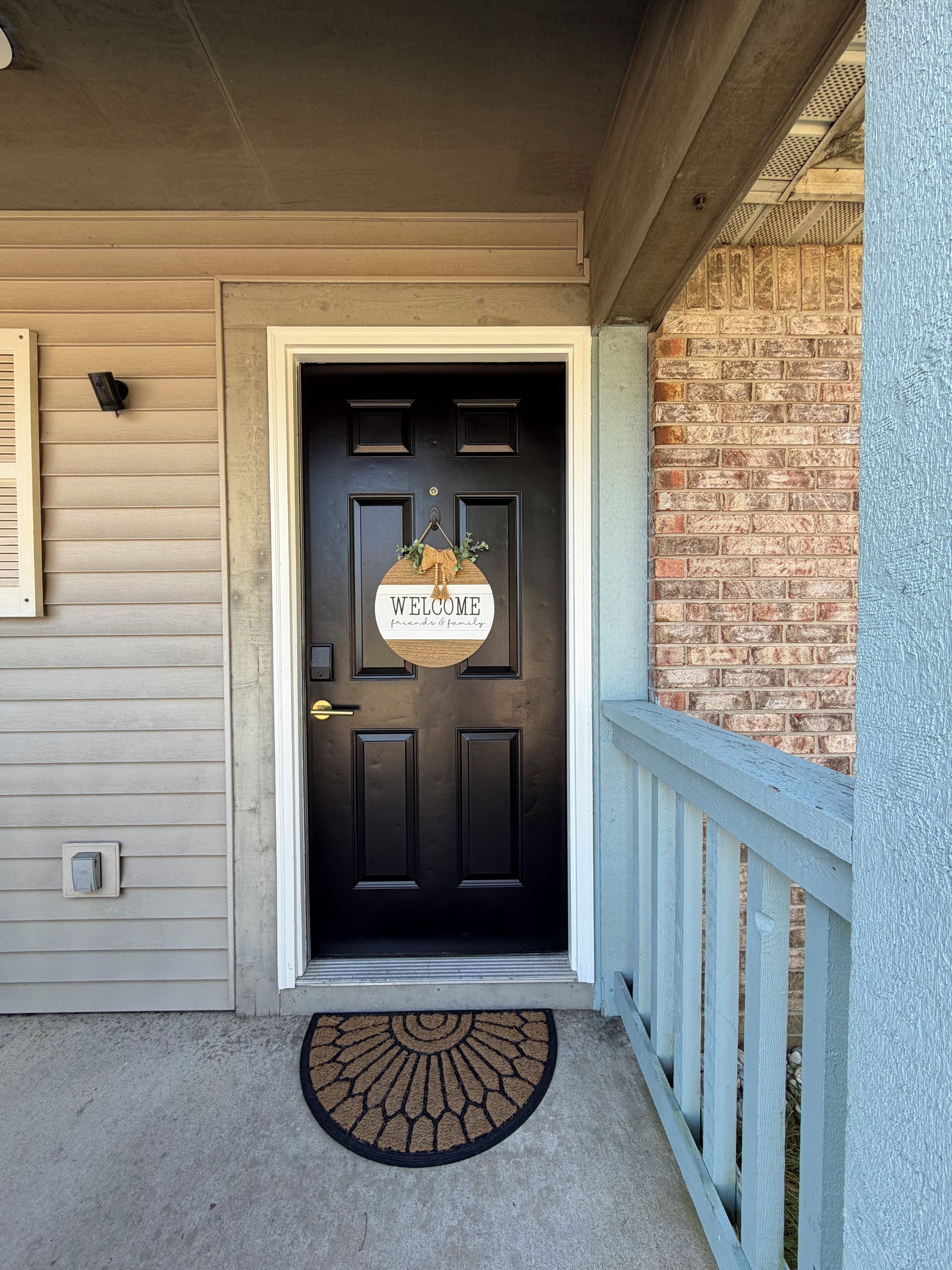 A black door with a welcome sign, a doormat, and a light blue railing.