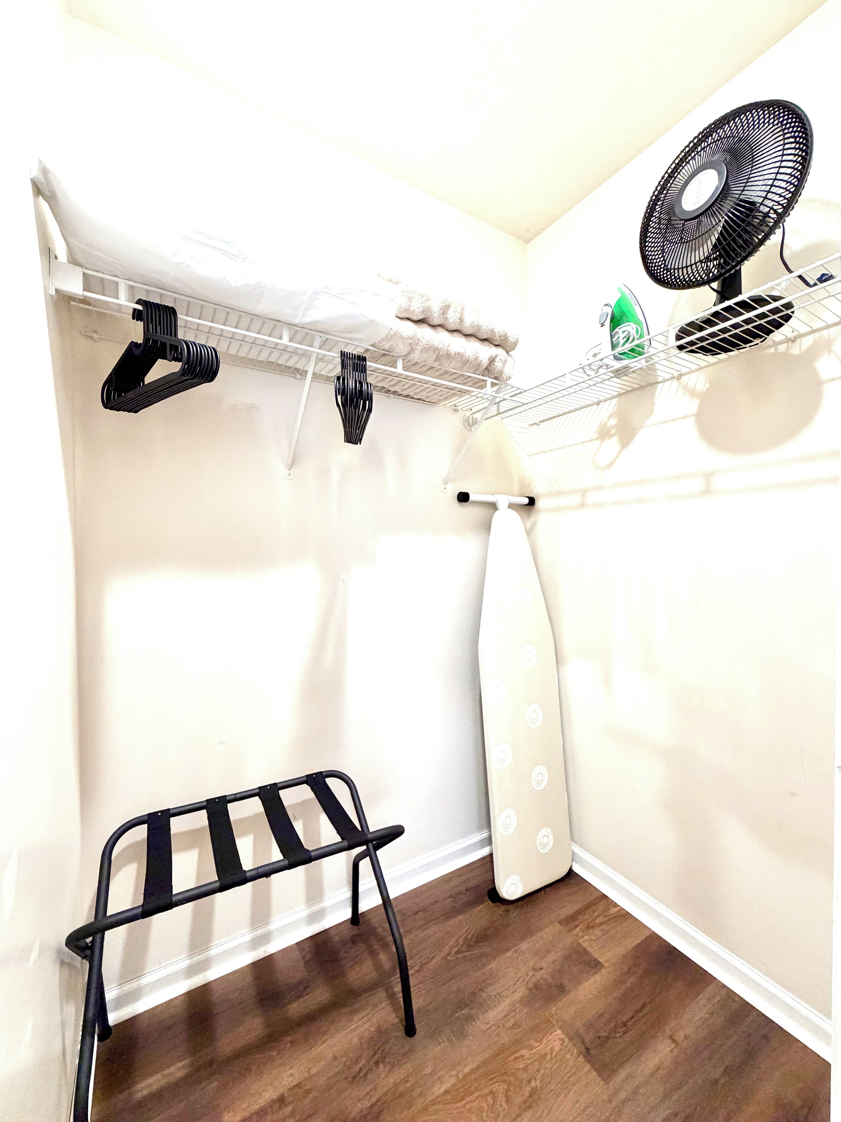 Un espace dédié à la lessive, comprenant un étendoir, des étagères avec des vêtements pliés et un ventilateur.
