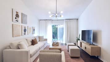 Una sala moderna con un sofá, un reposapiés y un televisor sobre un mueble de madera.