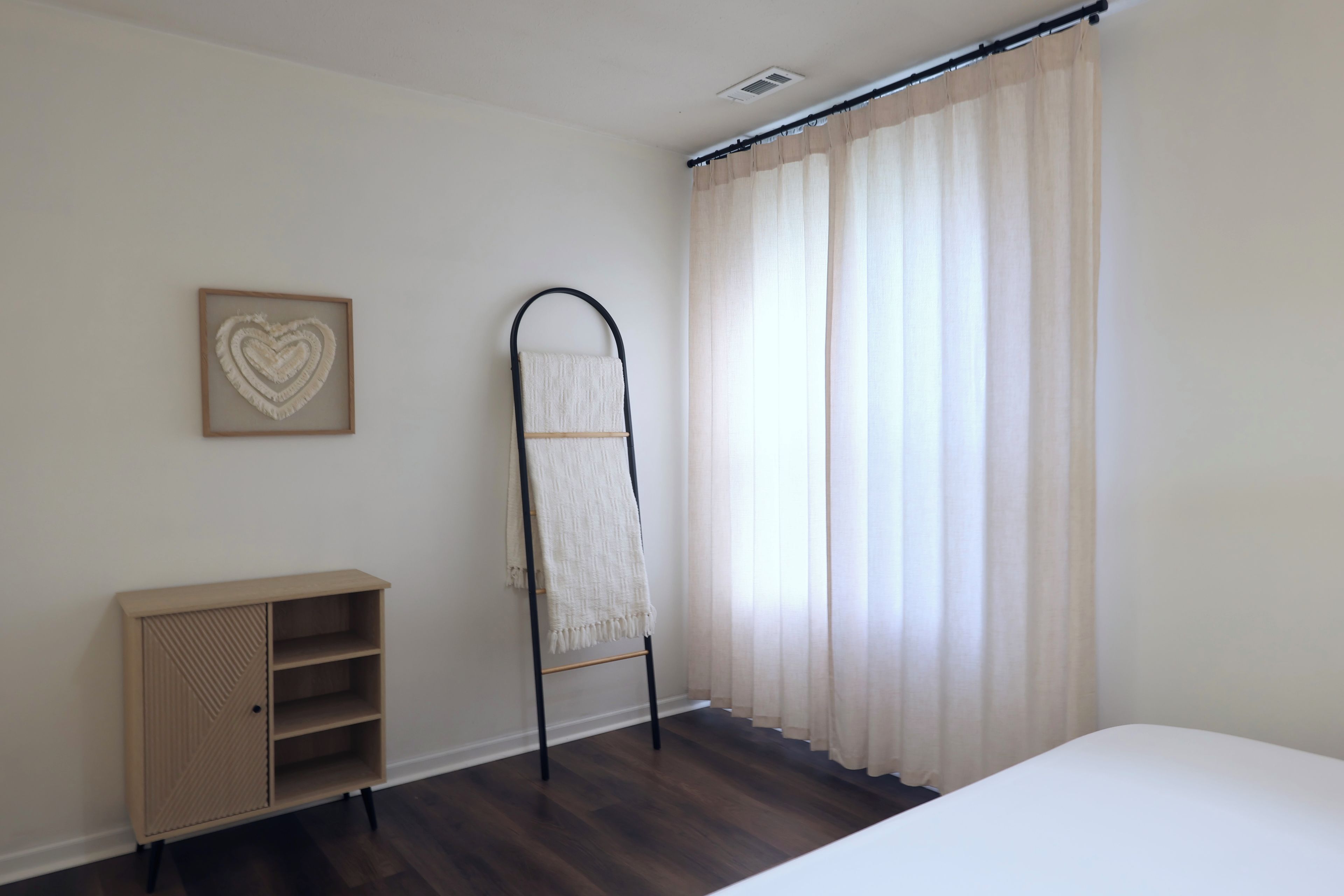 Ein Schlafzimmer mit einem Bett, einem Kleiderschrank, einem Wäscheständer und einem Fenster mit Vorhängen.