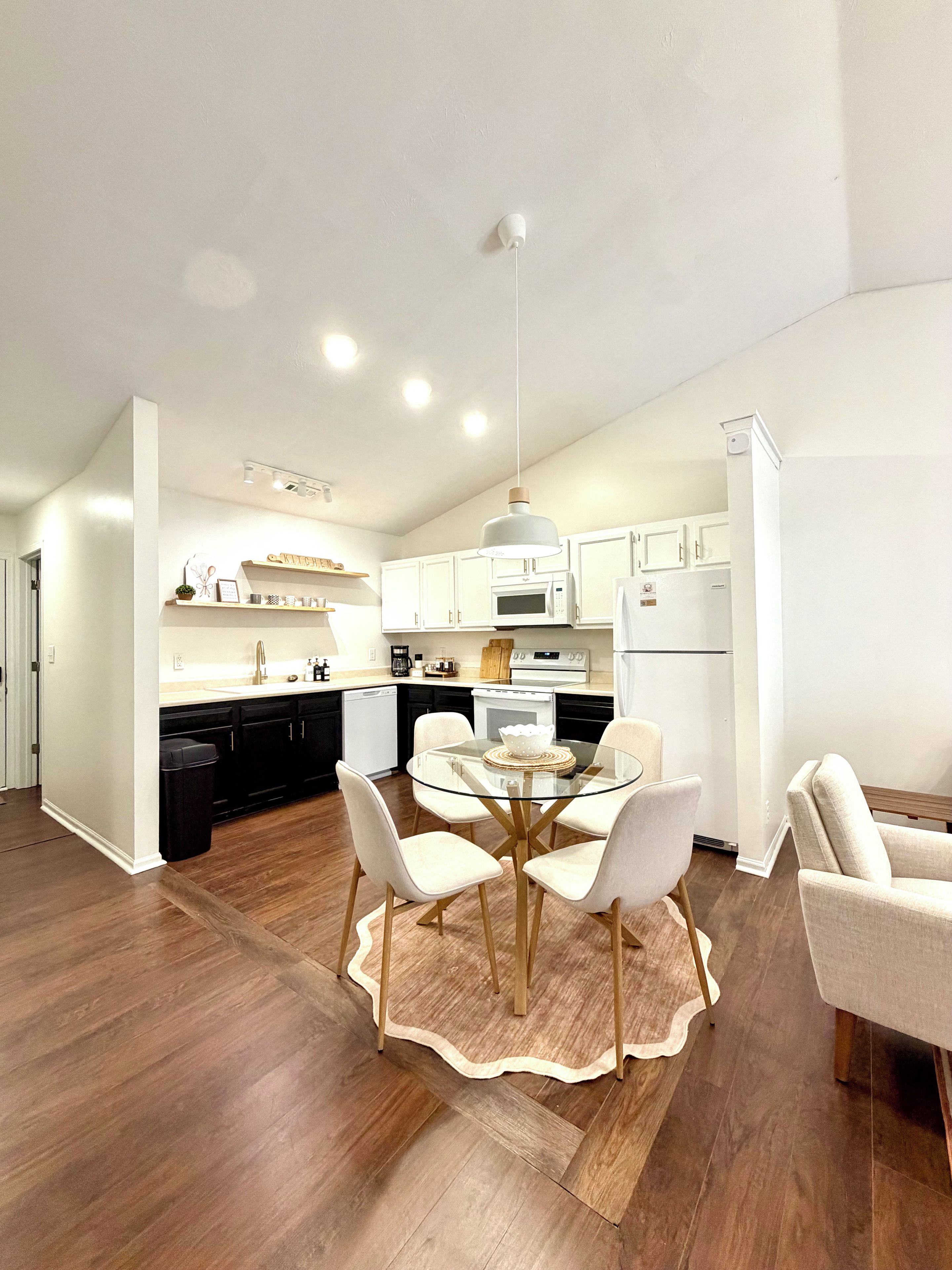 A modern kitchen with white cabinets, a central island, and a dining area with a glass table and chairs.