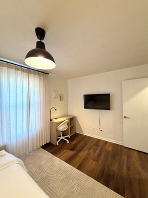 Habitación de hotel con una cama, un escritorio con silla, un televisor en la pared y una puerta.