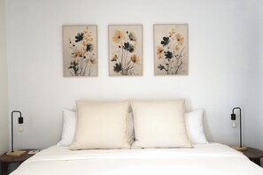 Un dormitorio con una cama, dos mesitas de noche y tres cuadros florales colgados en la pared.