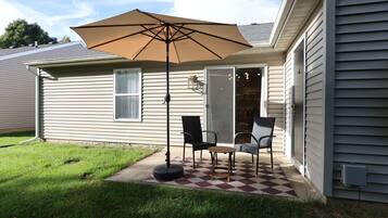 A house with a patio featuring two chairs and a table, a large umbrella, and a checkered floor.