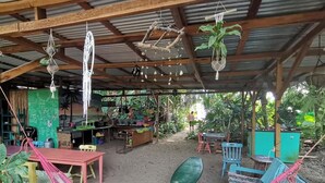 Uma área externa coberta com rede, mesas, cadeiras e plantas penduradas.