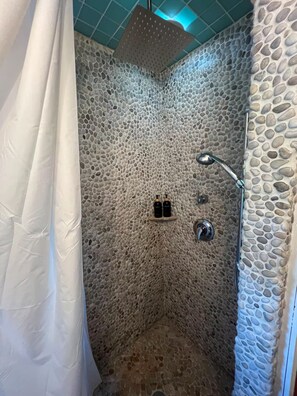 A shower with a stone wall, a showerhead, and a shelf with toiletries. - Large 3BR/2BA - 1500sqf - Steps to Harvard (Cambridge)
